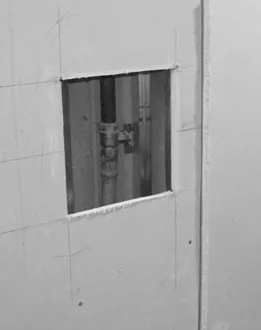 Вирізаний лобзиком отвір під люк у гіпсокартоні, видно комунікацію за отвором